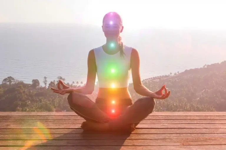 Mujer meditando frente al mar con chakras iluminados, representando el coaching holístico para el equilibrio energético en Mallorca.