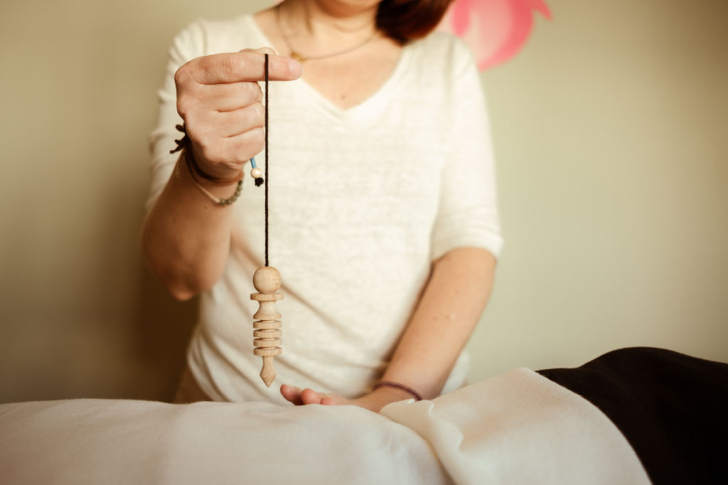 Cati Burguera utilizando un péndulo en un ritual de armonía corporal en Mallorca, equilibrando chakras y promoviendo el bienestar integral.